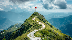 A winding dirt path leads up a lush green mountain ridge toward a red flag planted at the summit, with dramatic clouds and distant mountain ranges in the background.